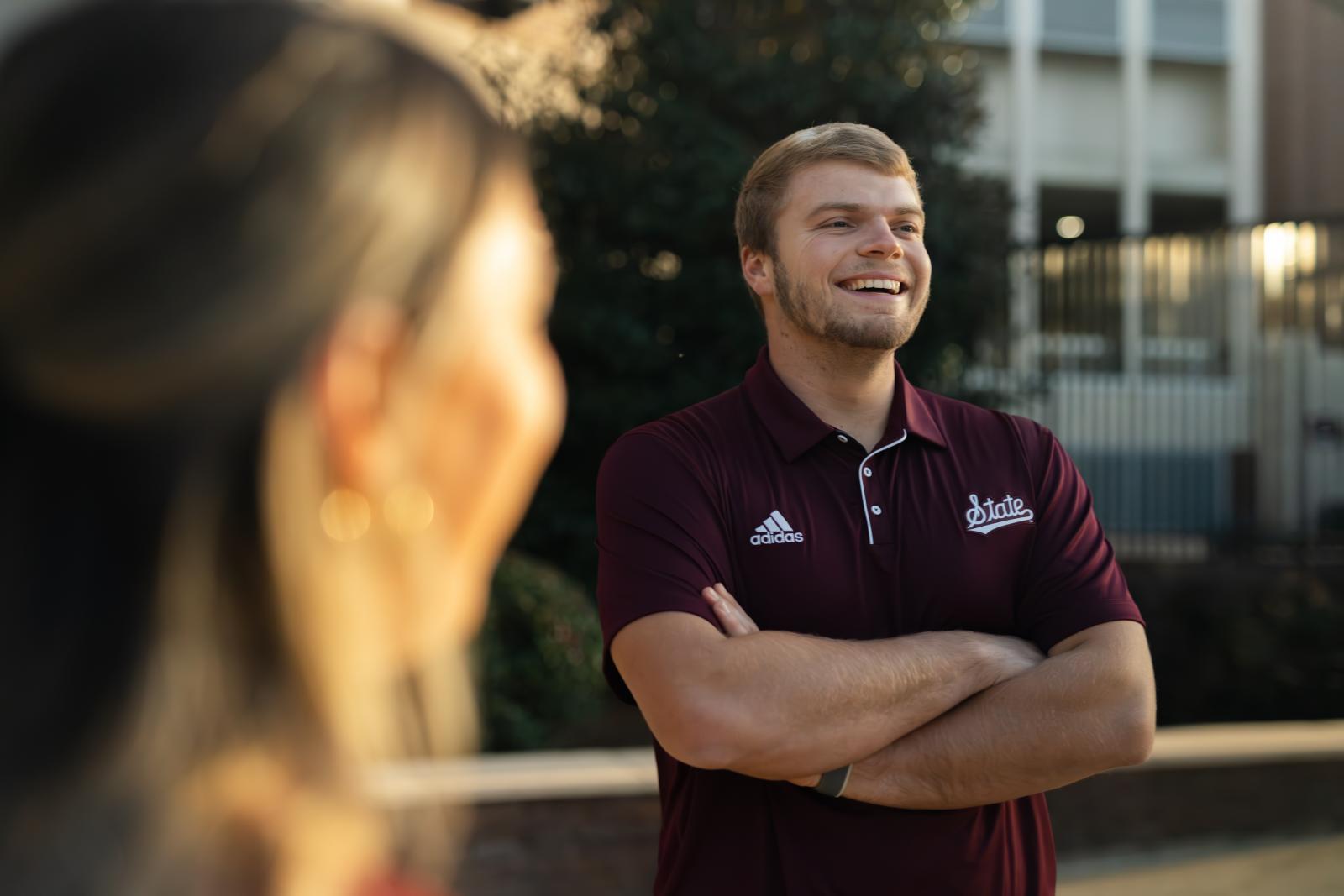 Student smiling with his arms crossed and wearing a maroon shirt.